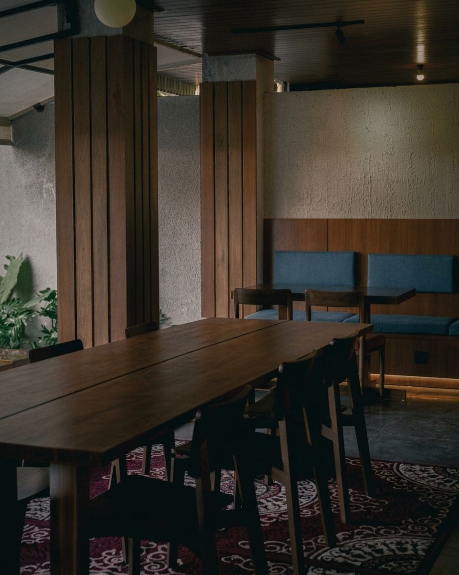 Un comedor con una larga mesa de madera, varias sillas y un banco con cojines azules.