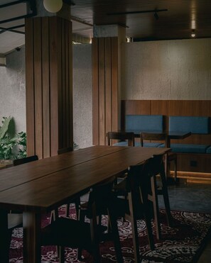 A dining area with a long wooden table, several chairs, and a bench with blue cushions. - Tedu Hotel (Canggu)