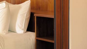 A bed with white bedding and pillows, a wooden headboard, and a small wooden shelf unit.