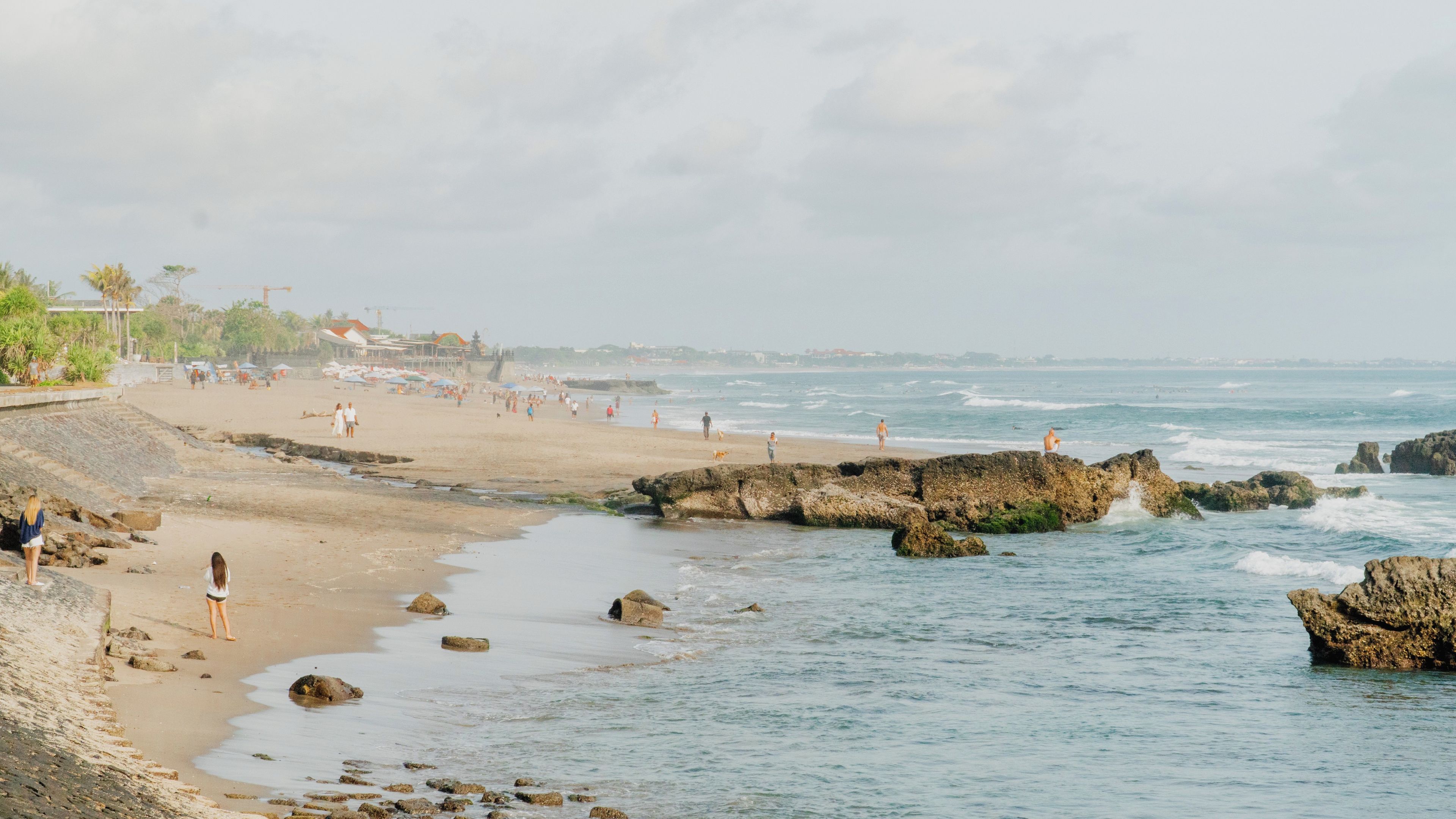 Una playa con afloramientos rocosos, gente caminando y un mar tranquilo.