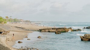 A beach with rocky outcrops, people walking, and a calm sea. - Tedu Hotel (Canggu)