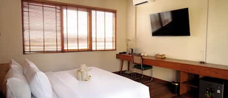 A hotel room with a bed, a desk, a chair, a television, and an air conditioning unit.
