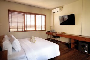 A hotel room with a bed, a desk, a chair, a television, and an air conditioning unit. - Tedu Hotel (Canggu)