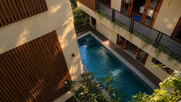 A modern building with a swimming pool, wooden slats, and a balcony with plants.