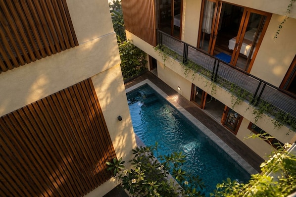 A modern building with a swimming pool, wooden slats, and a balcony with plants.