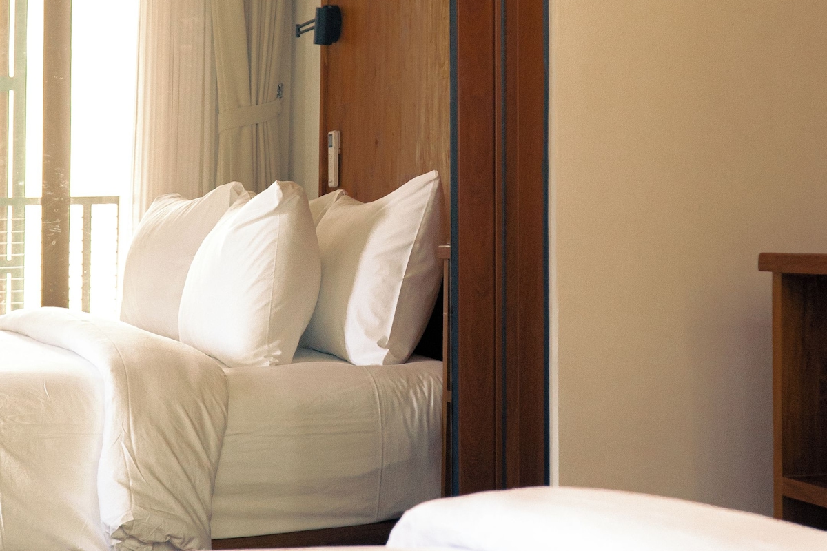 A hotel room with a bed, a wooden wardrobe, and a window with curtains.