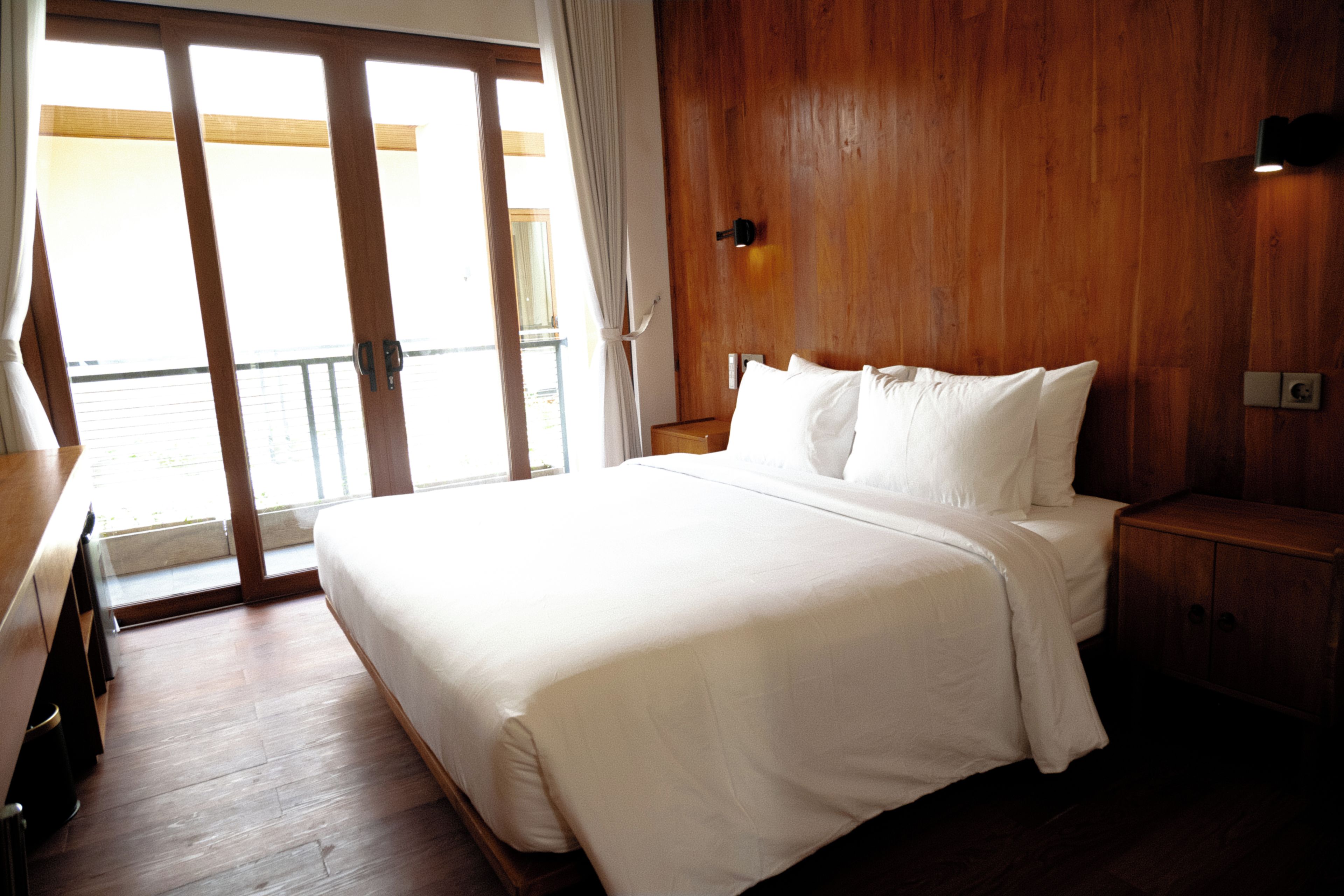 Habitación de hotel con una cama grande, paredes de madera, una ventana con cortinas y vistas al exterior.