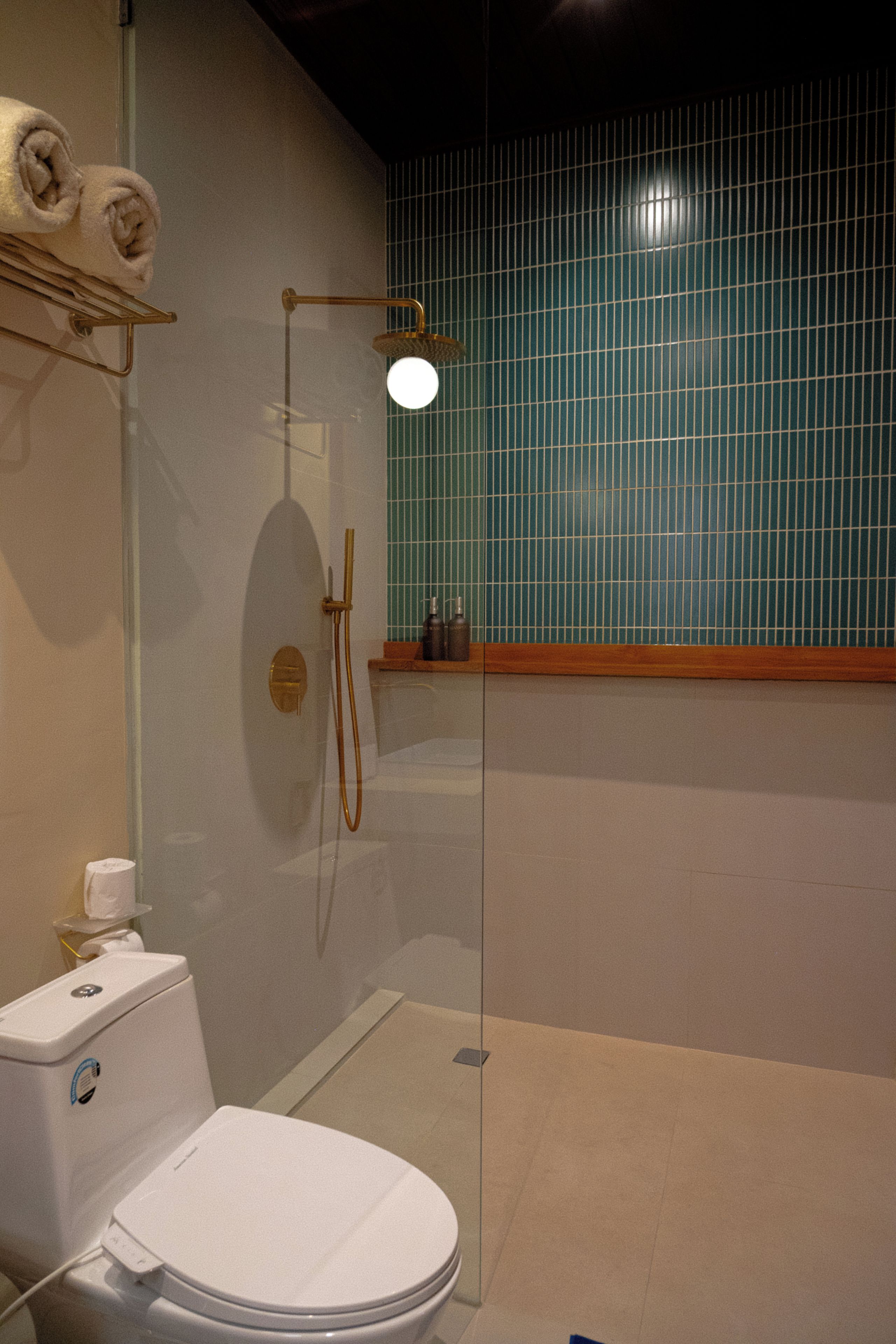 Un baño con inodoro blanco, ducha con cerramiento de vidrio y pared de azulejos.