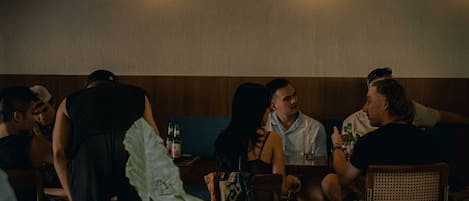 Un grupo de personas sentadas en una mesa en un ambiente interior con poca luz, pared lisa y dos luces en el techo.