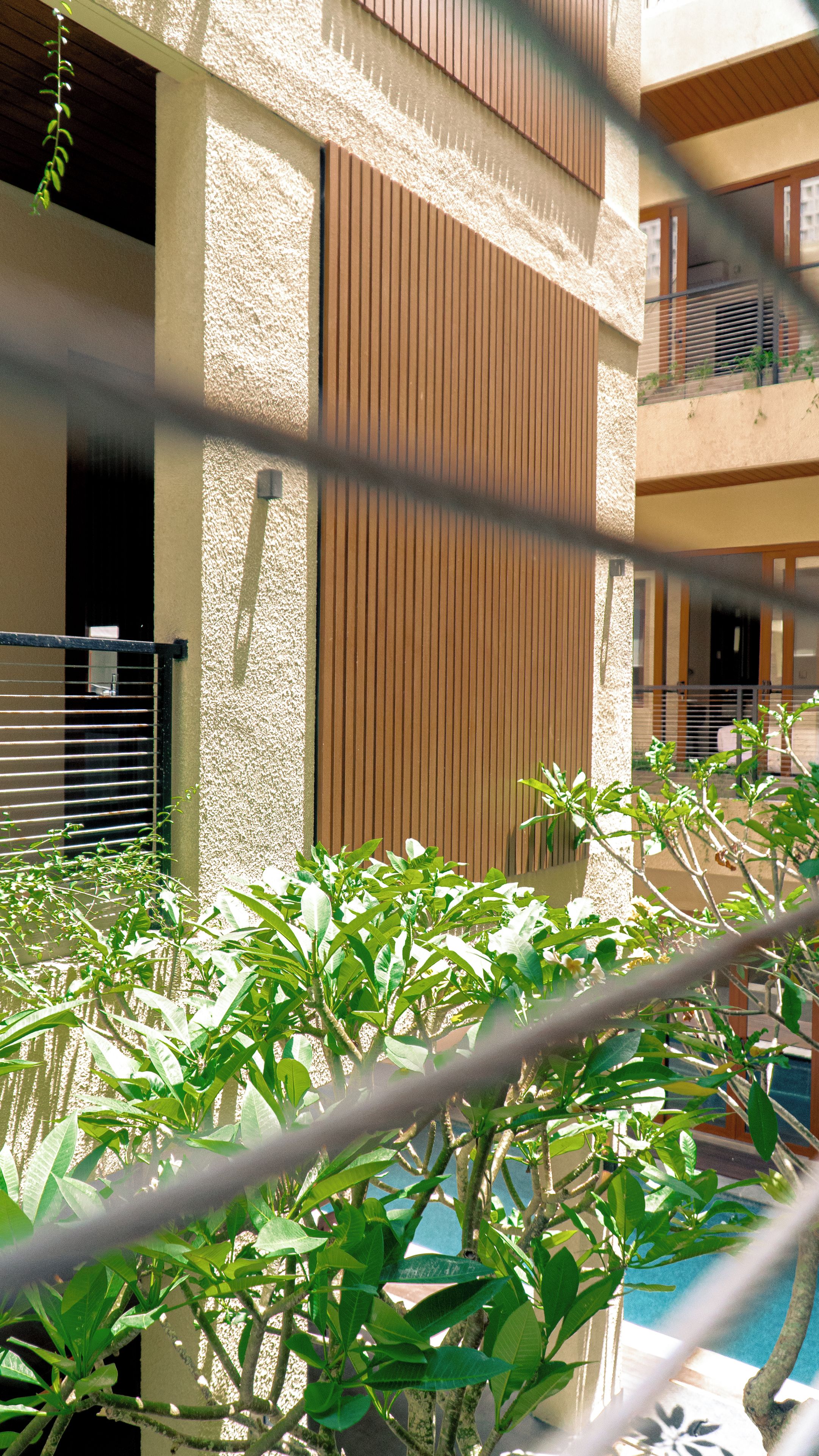 Ein Gebäude mit strukturierter Fassade, einem Balkon mit Geländer und einem Poolbereich mit Pflanzen.