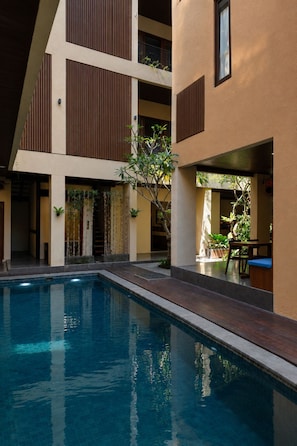 A modern building with a swimming pool, wooden slatted balconies, and indoor plants.