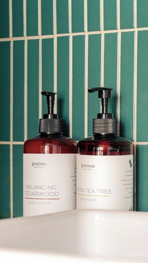 Twee flesjes bodylotion en handzeep op een wit oppervlak voor een groene betegelde muur.