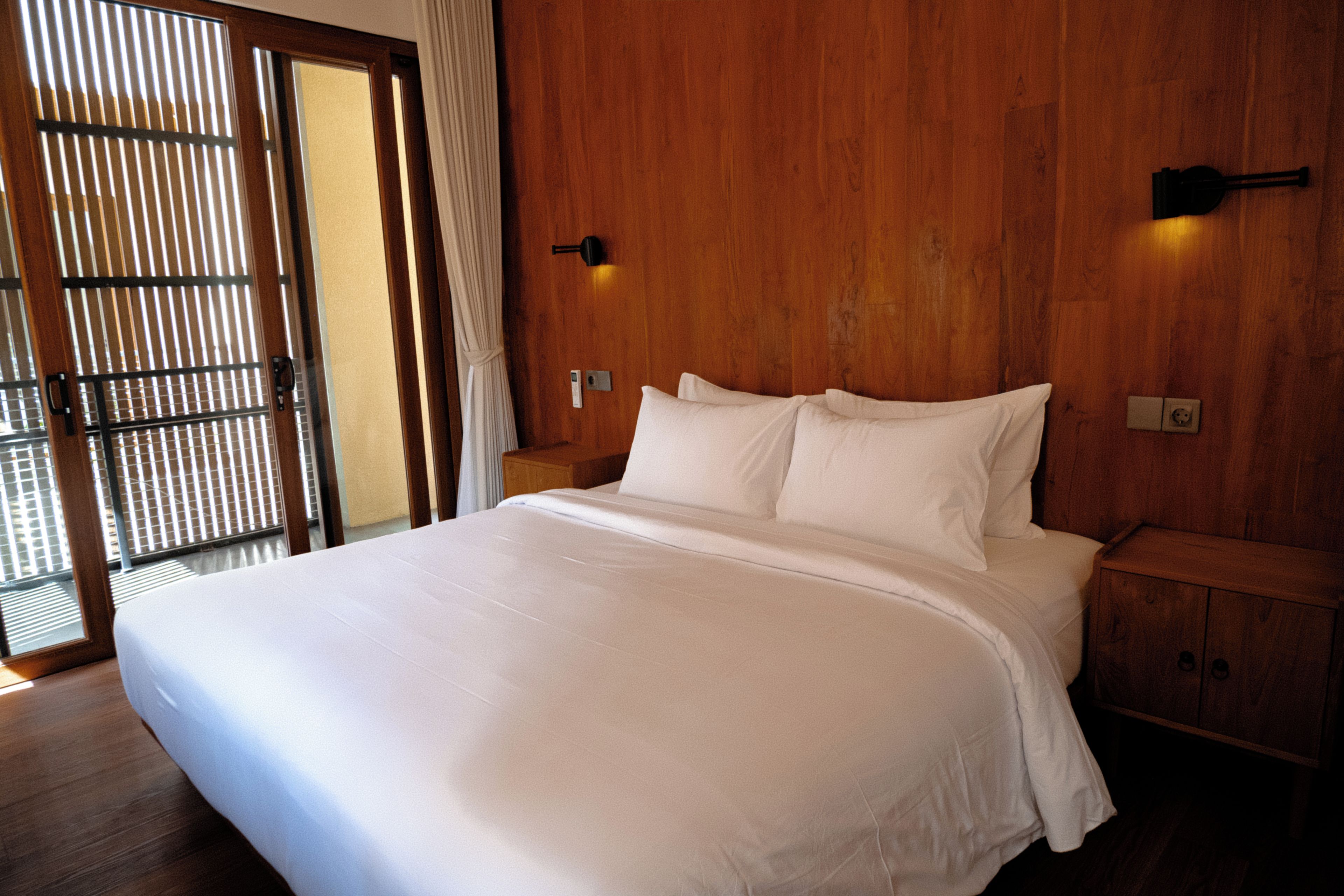 Ein Hotelzimmer mit einem großen Bett, einem Holzkopfende, einem Nachttisch und einer Wandleuchte.