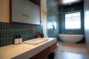 Een badkamer met een groot bad, een wastafel met twee kommen en een raam voor natuurlijk licht.