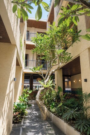 A multi-level outdoor atrium with a central tree, surrounded by various plants and a pathway. - Tedu Hotel (Canggu)