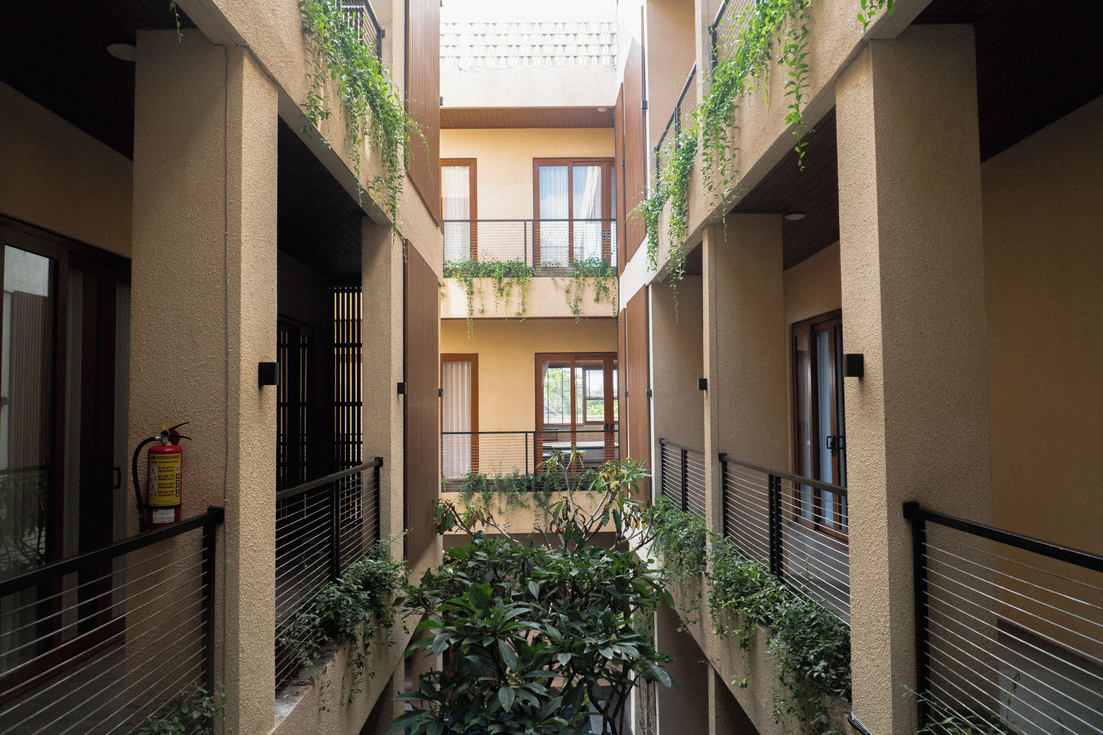 A multi-level residential building with balconies, a fire extinguisher, and a central courtyard with plants.