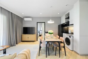 Ein modernes Wohnzimmer mit einem Flachbildfernseher, einem Essbereich mit Tisch für vier Personen und einer Küche inklusive Waschmaschine.