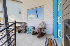Eine Veranda mit zwei Schaukelstühlen und einem kleinen Tisch, eine blaue Tür und ein Fenster mit Blick auf den Himmel.