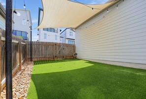 Ein Garten mit Kunstgrashalm, einem Holzzaun und einem Gebäude mit weißem Holzverkleidung.