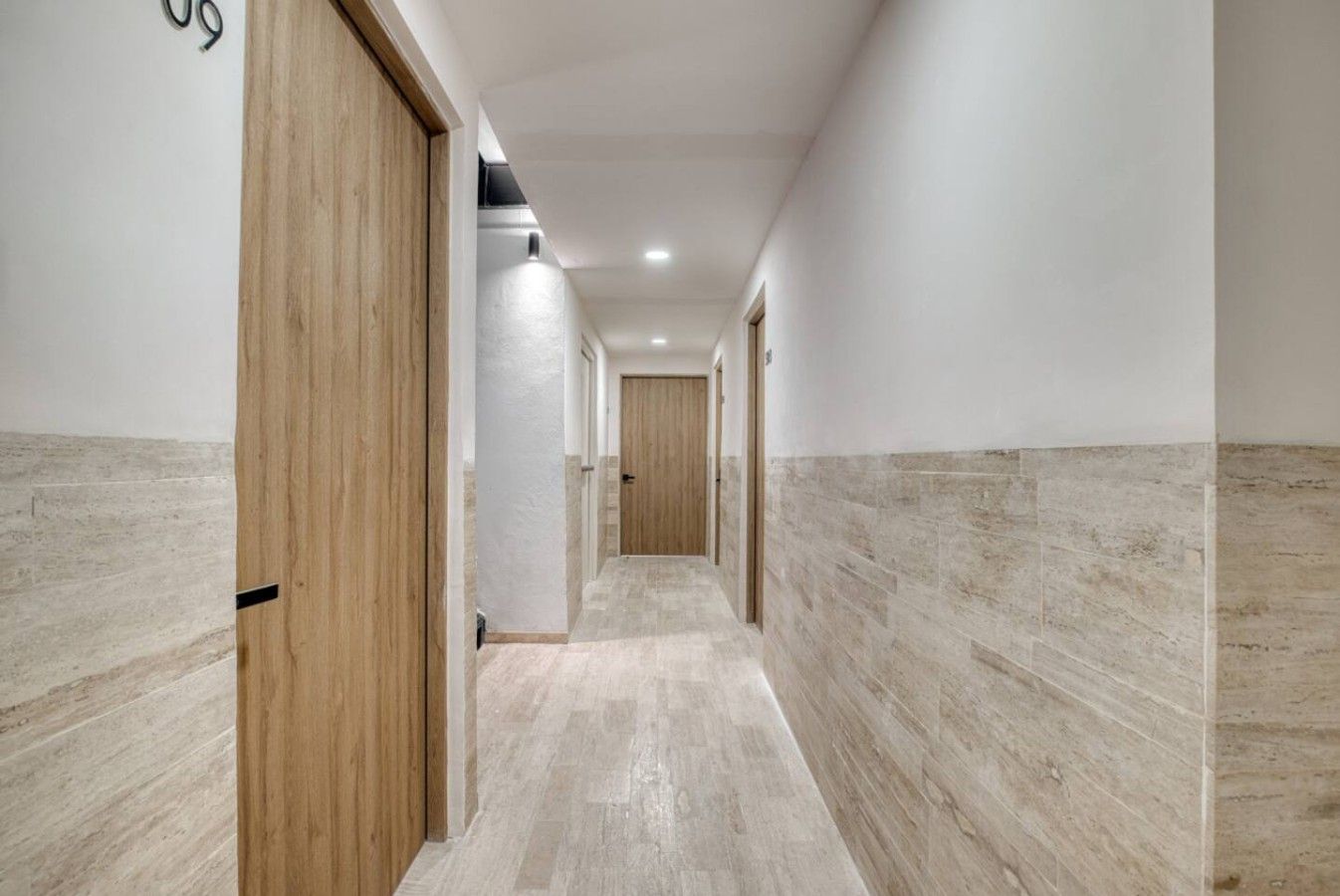 Un pasillo con puertas de madera y paredes con azulejos, que conduce a una habitación con una puerta al final.