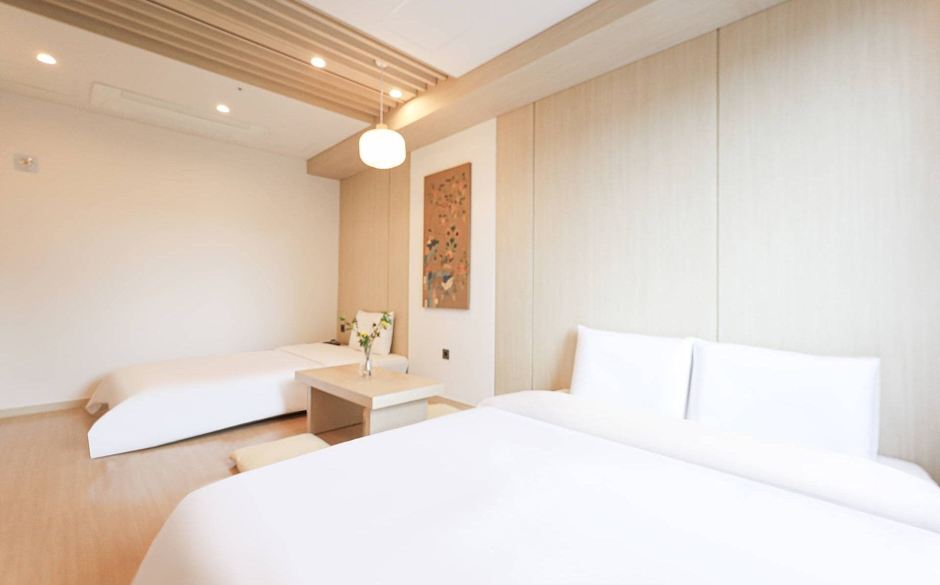 Habitación de hotel con dos camas, una mesita de noche con un florero y una obra de arte colgada en la pared.
