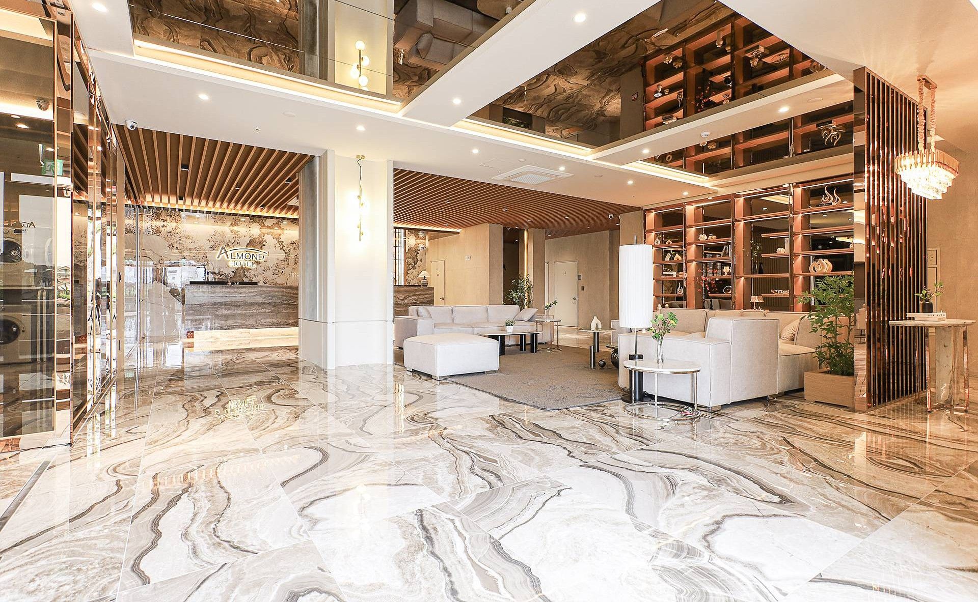 Un vestíbulo amplio con piso de mármol, un área de descanso con sofás y una gran estantería llena de objetos decorativos.