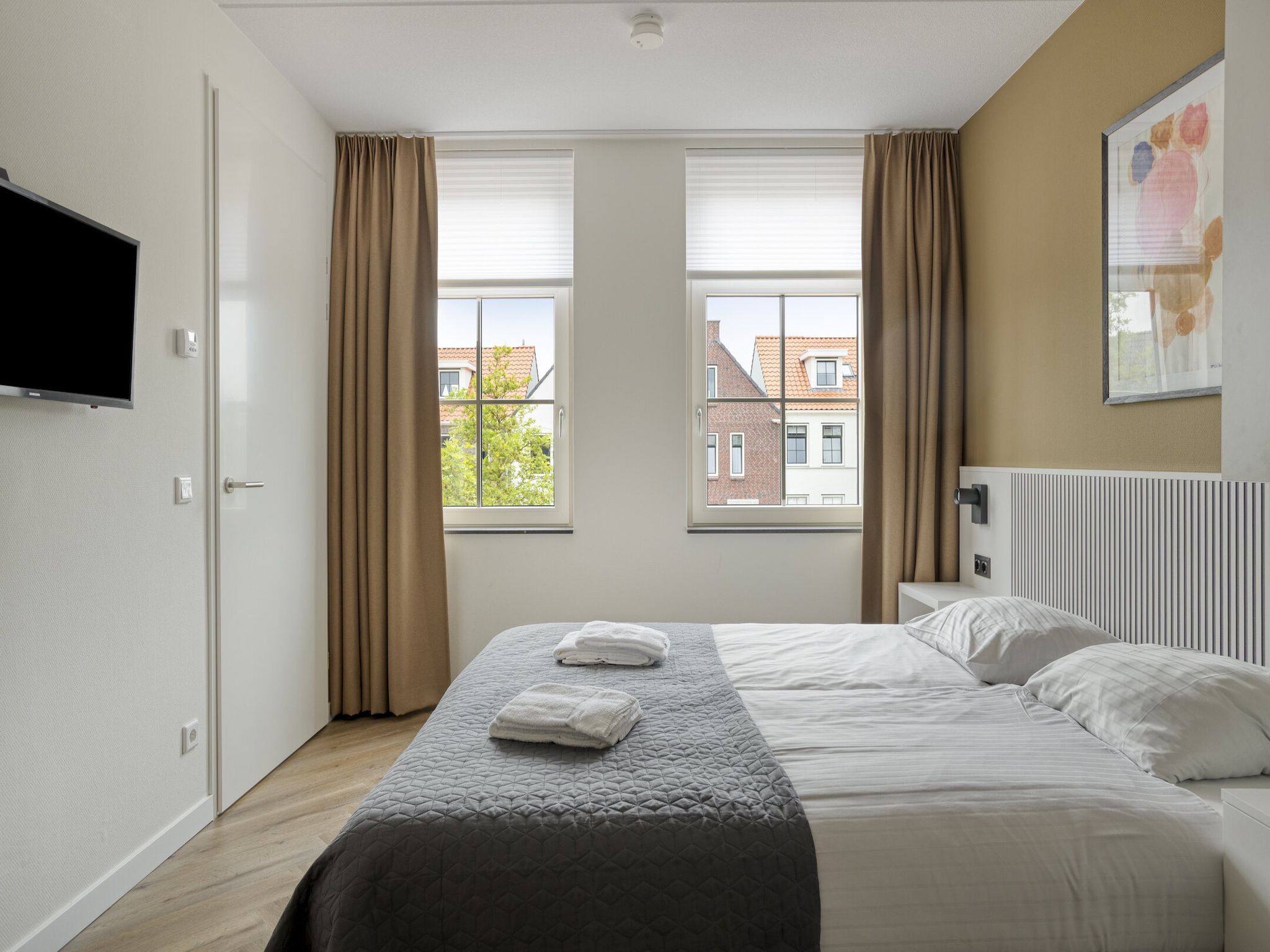 Et hotelværelse med seng, fladskærms-tv, radiator og et vindue med gardiner.