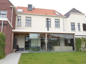 Ein zweistöckiges Haus mit überdachter Terrasse und Rasenfläche.