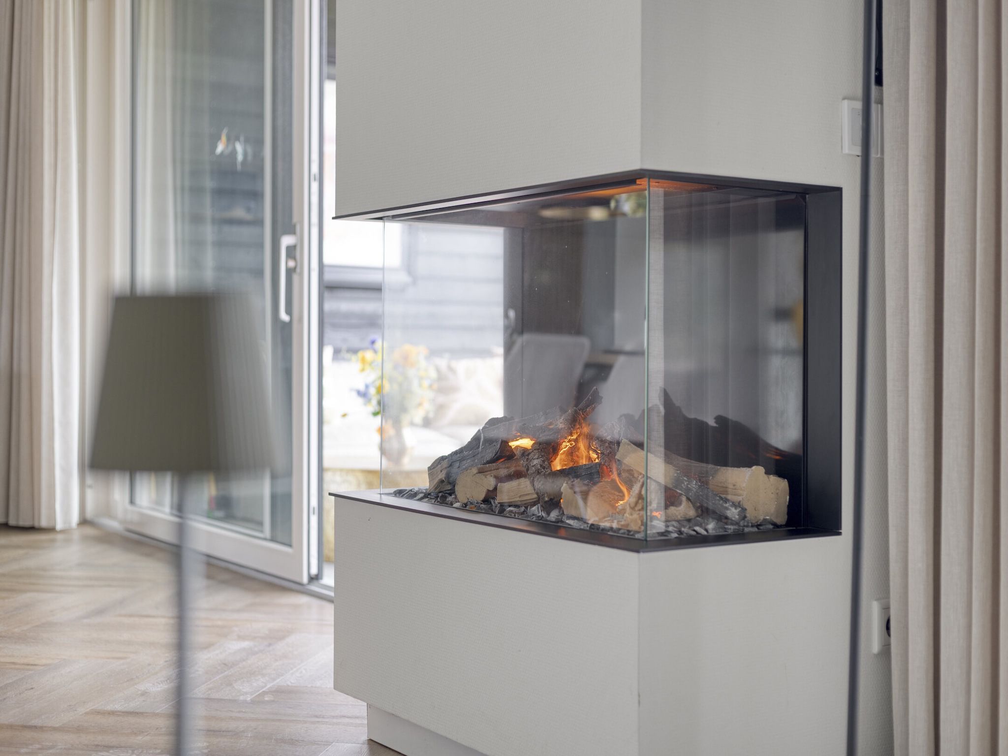 Ein moderner Kamin mit Glaseinfassung, platziert in einer Ecke des Raumes mit einer Schiebetür aus Glas.