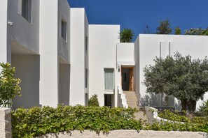 Ein modernes Gebäude mit einer hellen, weißen Fassade, einer sichtbaren Treppe zum Eingang und einem gepflegten Heckenstreifen im Vordergrund.