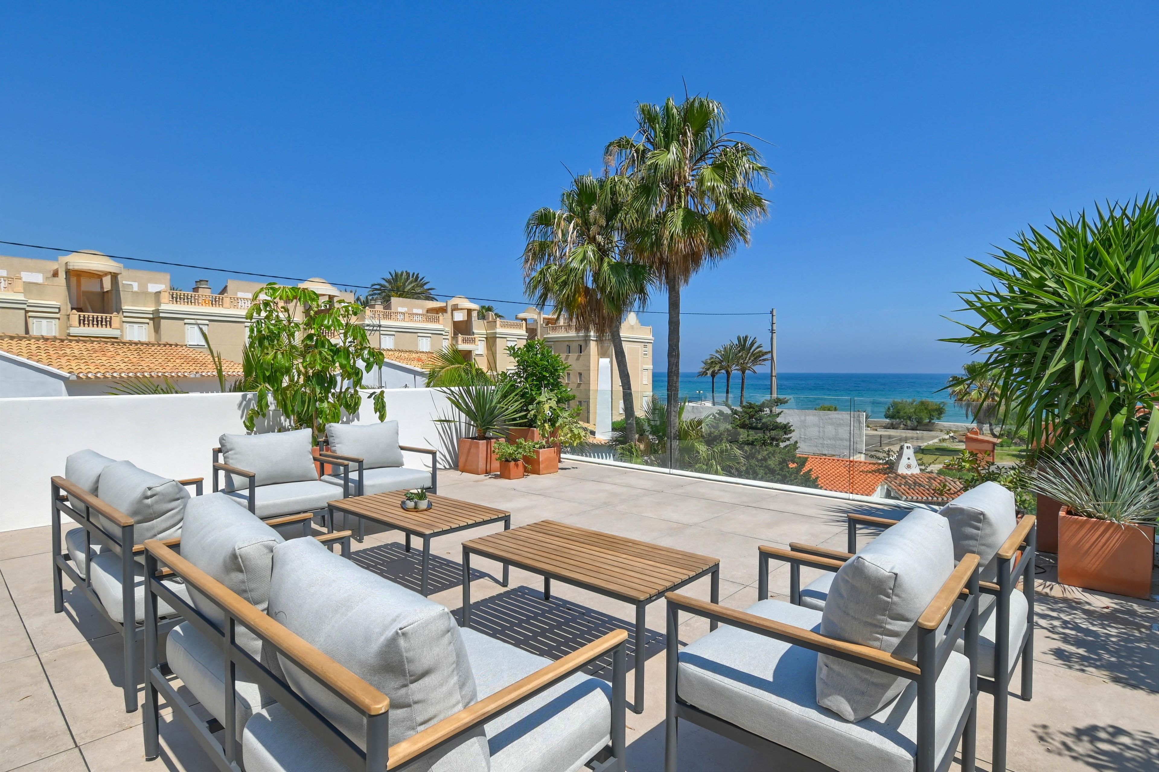 Eine Dachterrasse mit Außenmöbeln, Blumentöpfen und Blick auf das Meer.