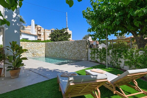 Ein Garten mit Swimmingpool, Steinmauer und Liegestühlen.