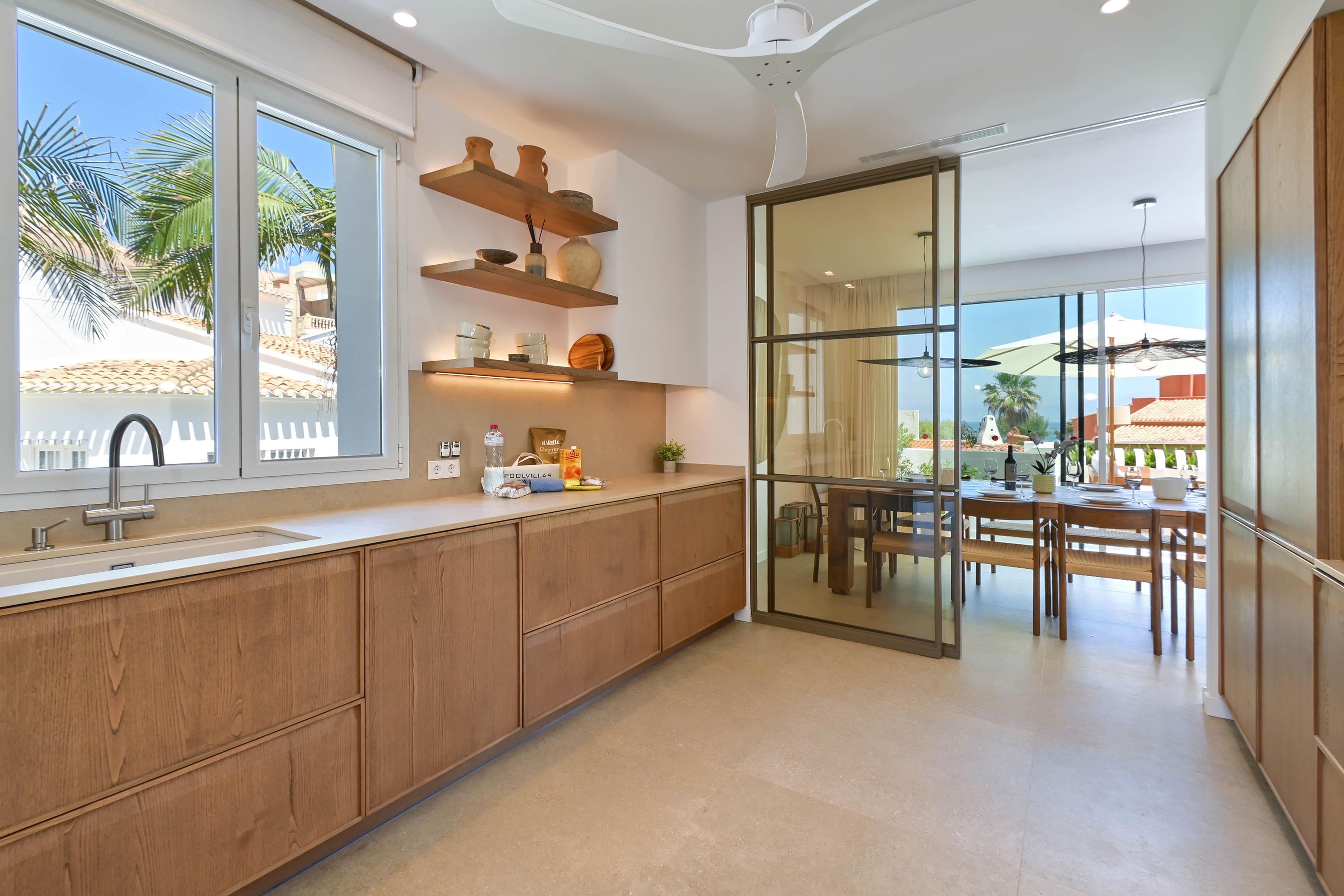 A modern kitchen with wooden cabinets, a built-in oven, and a large window overlooking a patio area.
