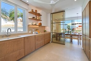 A modern kitchen with wooden cabinets, a built-in oven, and a large window overlooking a patio area. - El Jabeque 4 pax - Denia, Costa Blanca (Denia)
