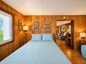 Ein Schlafzimmer mit einem großen Bett, einem Schreibtisch und einem Sessel. Ein Fenster befindet sich links und eine Tür führt in einen anderen Raum.