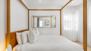 A bedroom with a large bed, a wooden headboard, a mirror, and a window with sheer curtains. - Riva House - Exquisite 4-bedroom holiday house (Gwandalan)