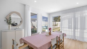 A modern dining area with a table set for two, a white console table with a mirror and a vase, and a view of a swimming pool through large windows. - Riva House - Exquisite 4-bedroom holiday house (Gwandalan)