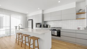 A modern kitchen with a central island, bar stools, a built-in oven, and a coffee machine. - Riva House - Exquisite 4-bedroom holiday house (Gwandalan)