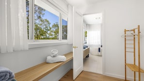 A modern bathroom with a wooden bench, a towel, and a view of the outdoors through a window. - Riva House - Exquisite 4-bedroom holiday house (Gwandalan)