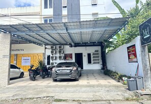 A building with a covered entrance, a parked car, and several motorcycles. - Cozy Solo Room at Medina House (Banda Aceh)