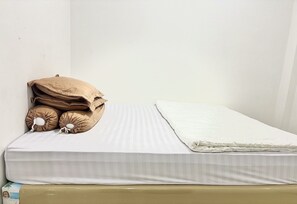 A single bed with a white mattress and a beige blanket, accompanied by two brown pillows with a drawstring. - Cozy Solo Room at Medina House (Banda Aceh)