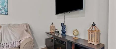 A living room with a flat-screen TV mounted on the wall, a fireplace, a sofa, and a console table with decorative items.