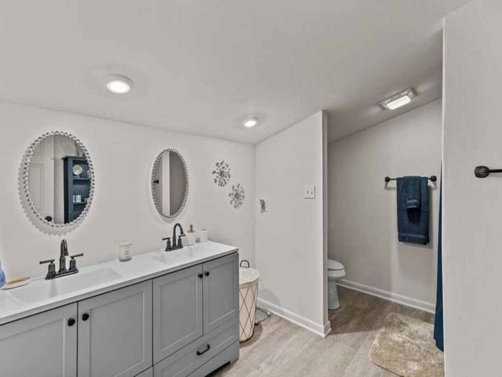 A bathroom with a double vanity, two mirrors, a toilet, and a towel rack.