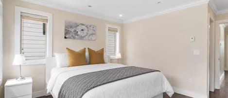 A bedroom with a bed, two bedside tables, a window with blinds, a ceiling light, and a wall-mounted artwork.