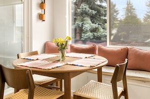 A round wooden table with woven chairs, a pink cushioned bench, and a vase with yellow flowers. - Private Softub, Walk to Junction - 2BR + Den, King Bed (Seattle)