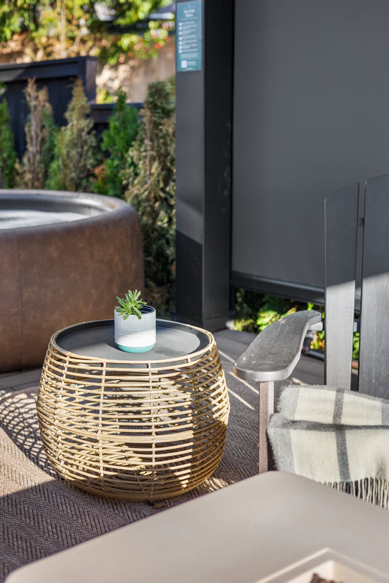 A wicker round table with a glass top and a small potted plant, a cushioned chair, and a large planter with a plant.
