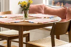 A round wooden table with a pink cushion, a vase with yellow flowers, and woven placemats. - Private Softub, Walk to Junction - 2BR + Den, King Bed (Seattle)