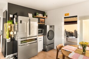 A modern kitchen with a refrigerator, microwave, oven, and dishwasher. There is a dining area with a table and chairs. - Private Softub, Walk to Junction - 2BR + Den, King Bed (Seattle)