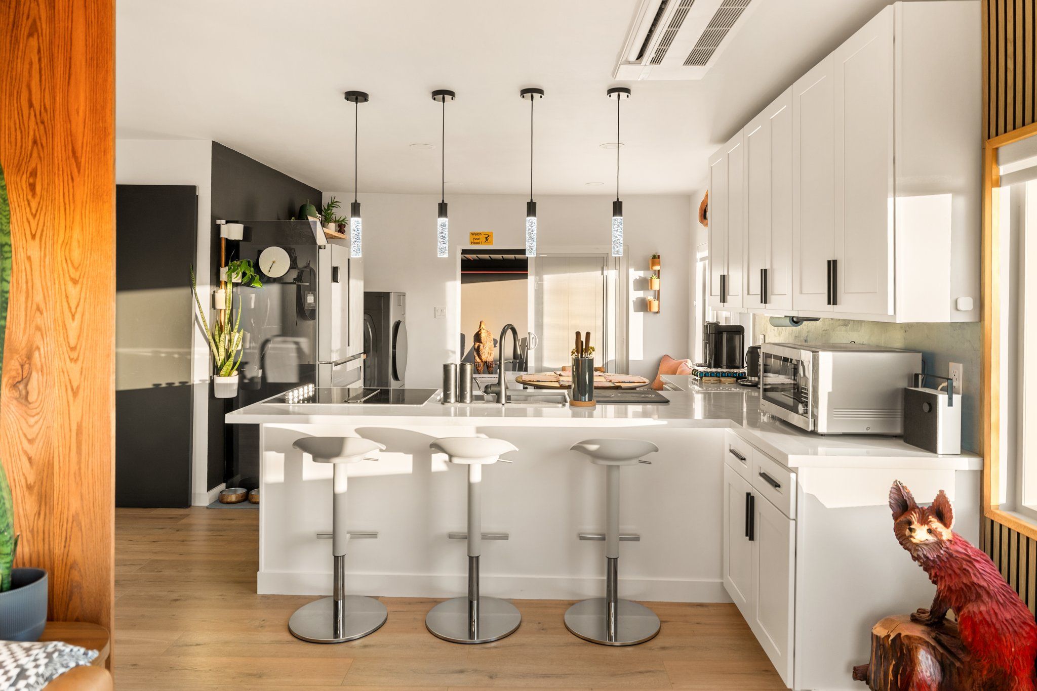 A modern kitchen with a central island, bar stools, and a microwave.
