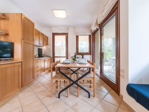 A compact kitchen with wooden cabinets, a dining table with chairs, and a TV on the left. - Vacation home Carlo by Interhome (Villasimius)
